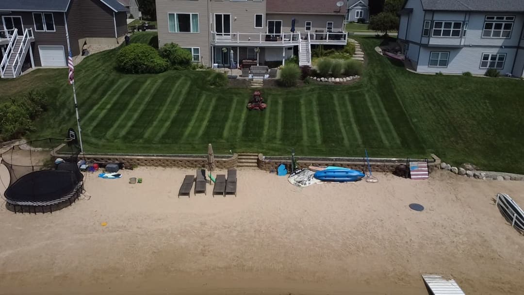 Lawn and beach area with patio furniture, kayaks, and a waterfront house in summer.