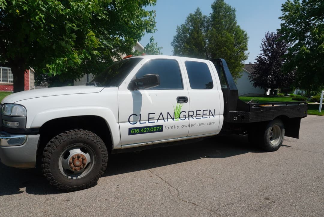 Clean Green lawn care service truck parked on a residential street with green landscaping.