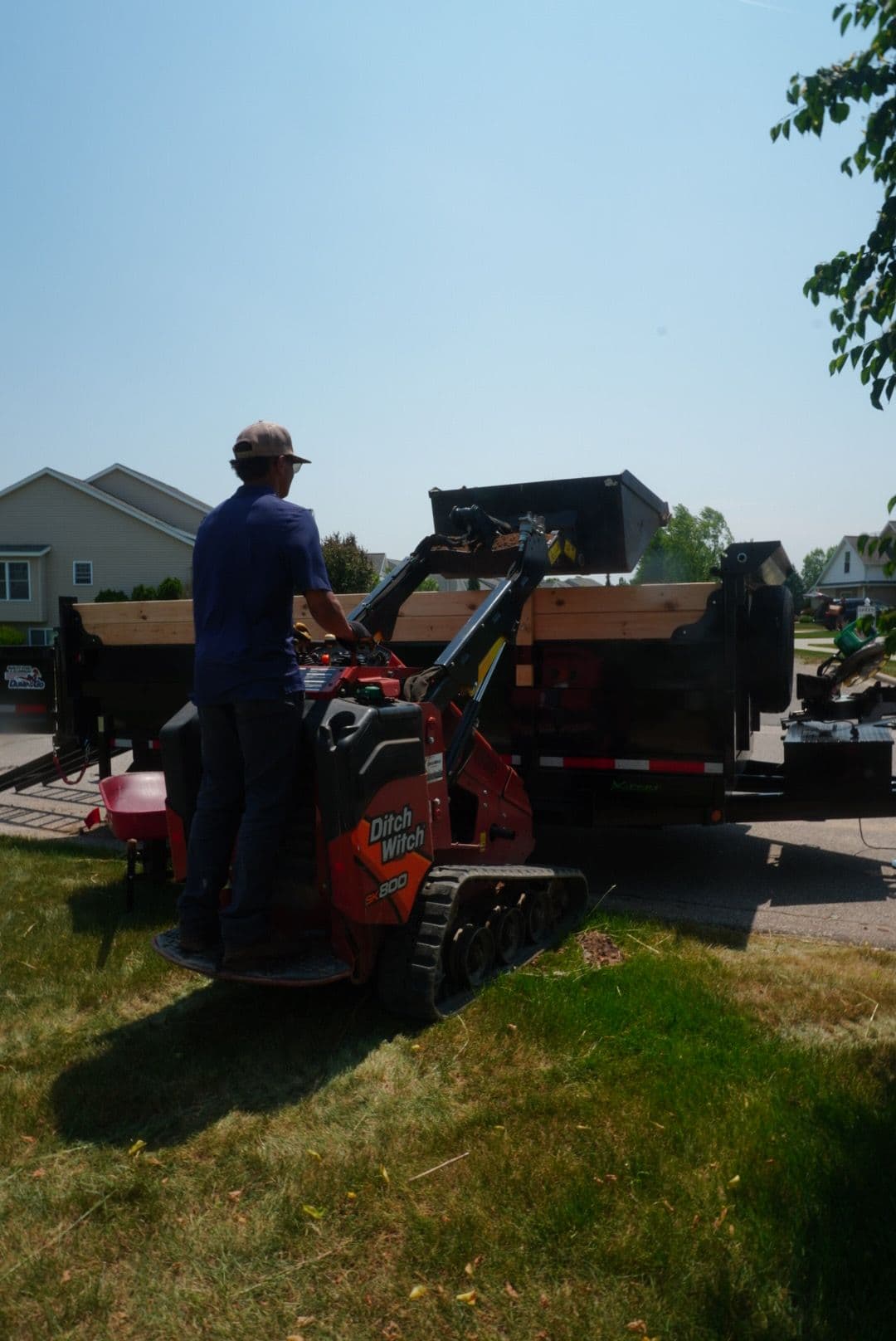 Person operating a Ditch Witch mini skid steer loader on a residential lawn.