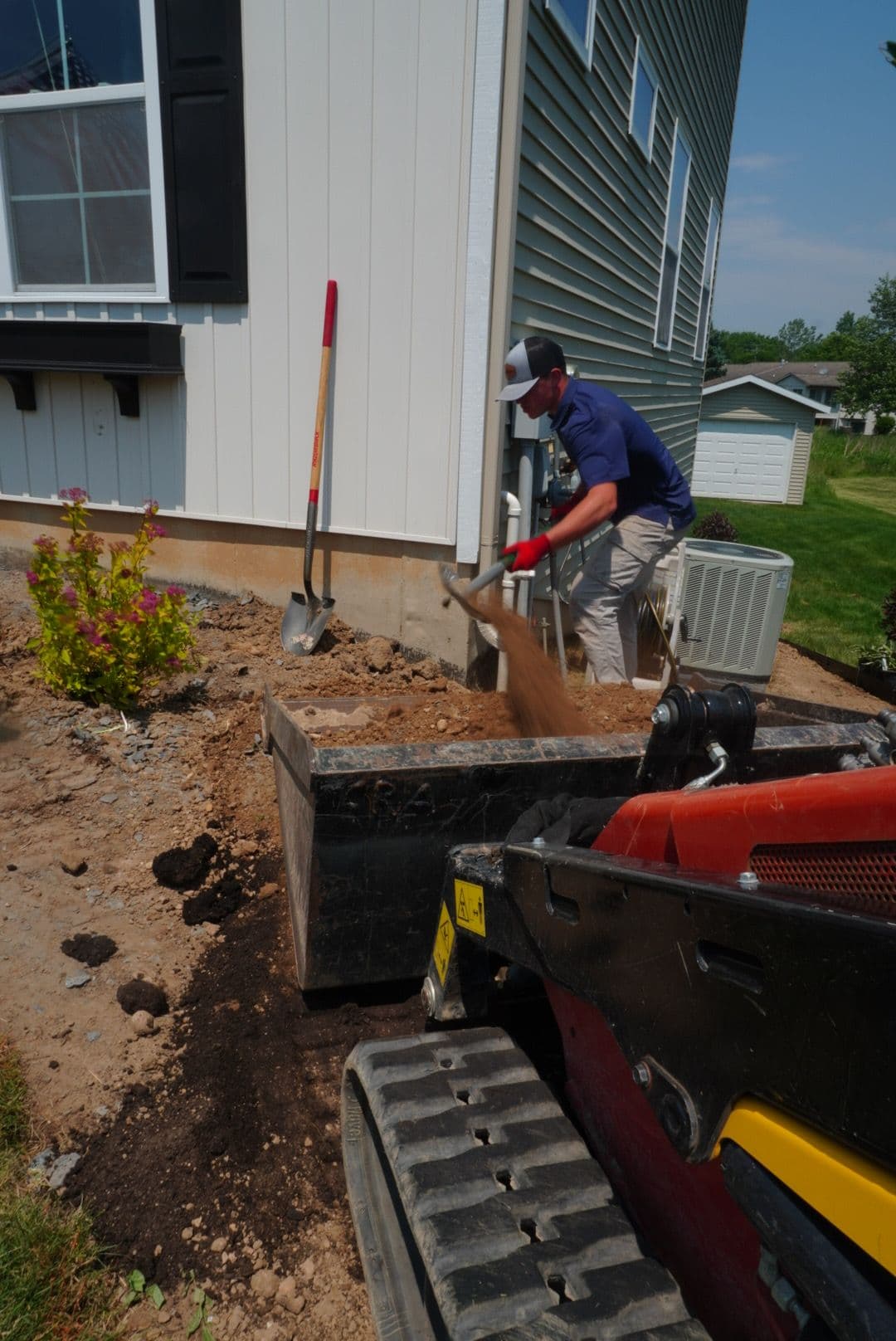 Construction worker using a skid steer to move soil near a house foundation.