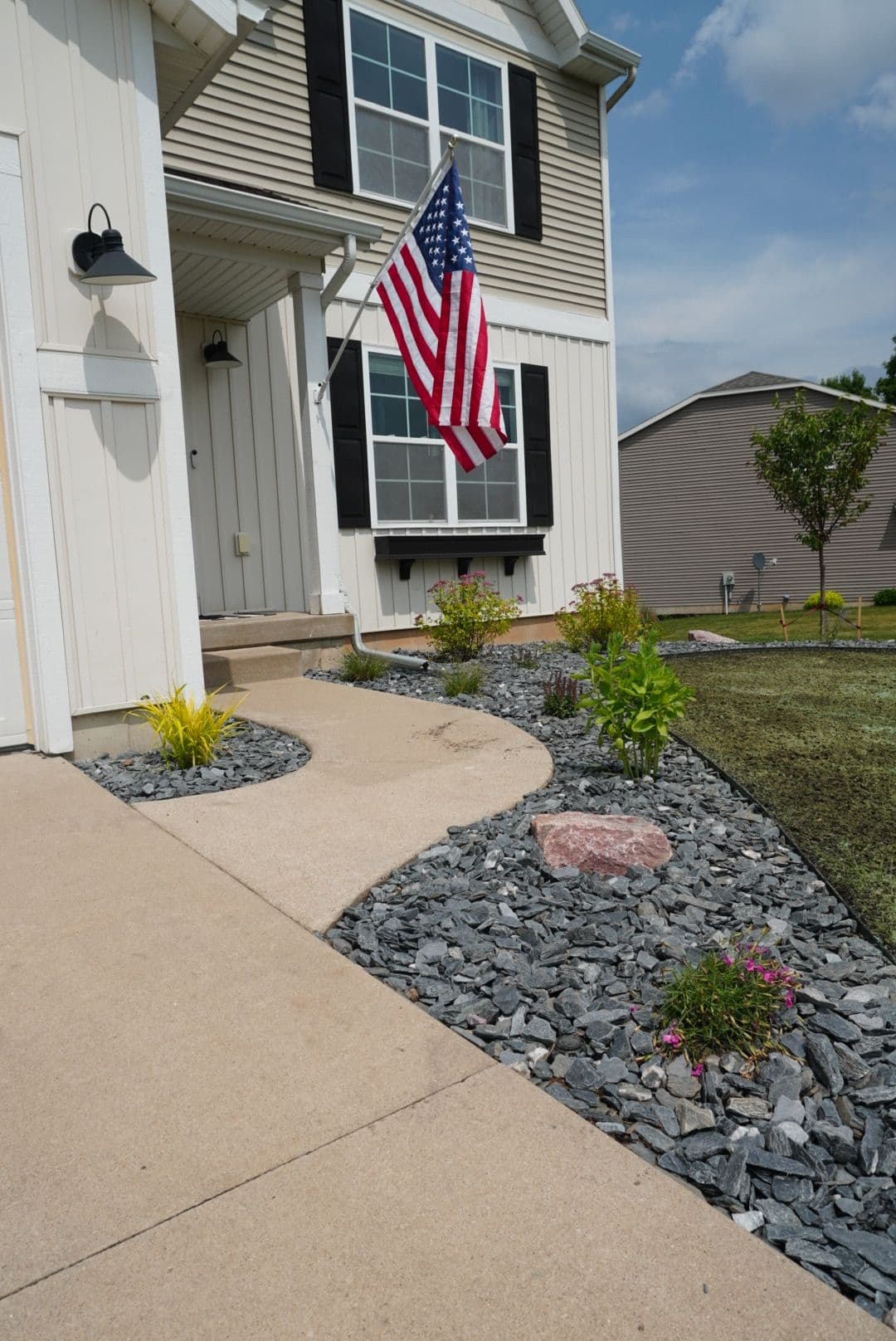 American flag adorns a charming home entrance with a landscaped path and colorful flowers.