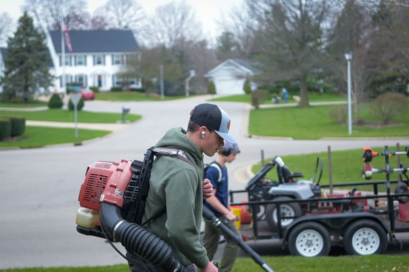 Landscapers using backpack blowers in a residential neighborhood with landscaping equipment.