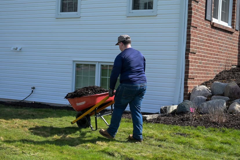 Person using a wheelbarrow to transport mulch in a residential yard.